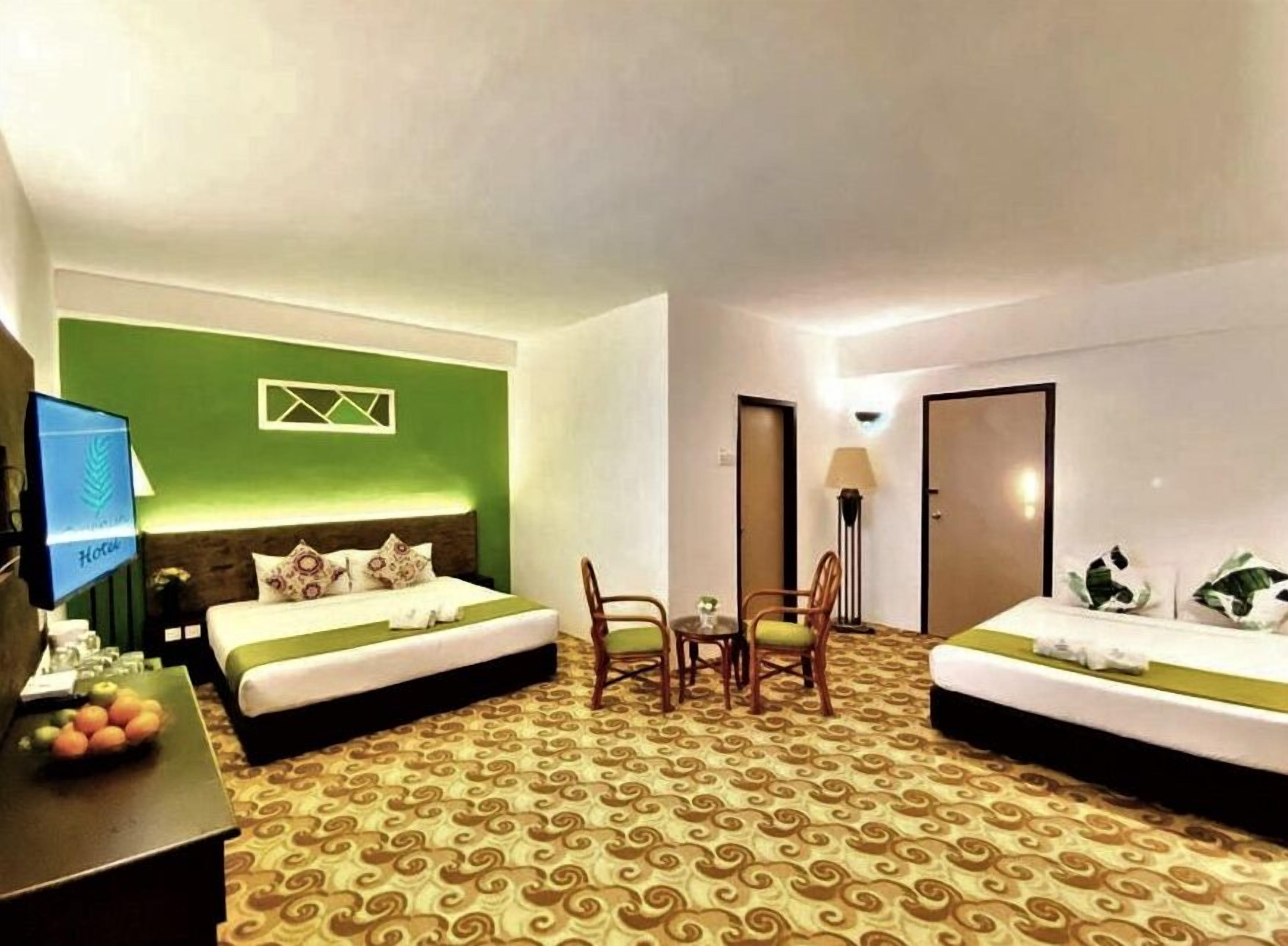 Habitación de hotel con dos camas, un escritorio y una televisión, además de una alfombra estampada.