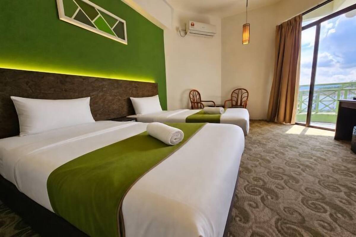 Une chambre d’hôtel avec deux lits, un mur d’accent vert, une grande fenêtre avec vue et un ventilateur de plafond.