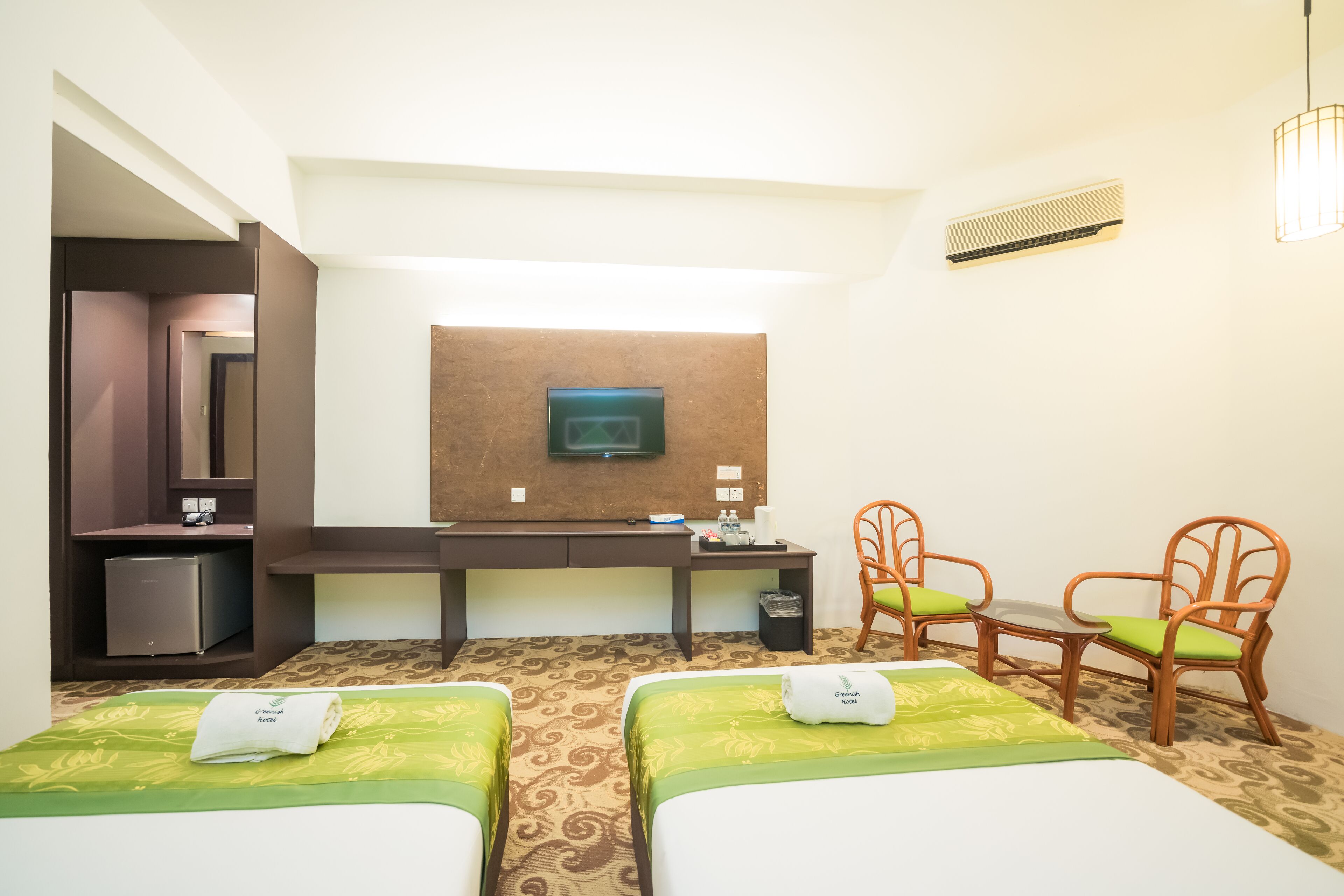 A hotel room with two beds, a desk, a television, and a small refrigerator.