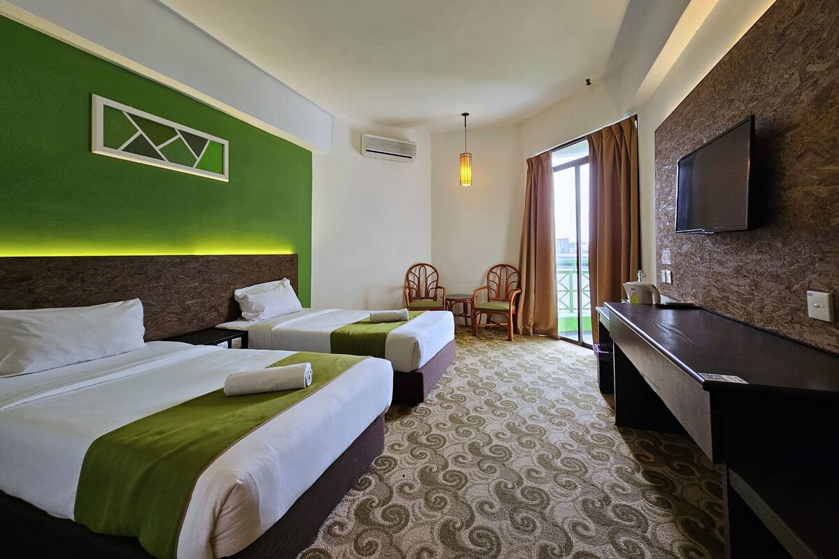 Une chambre d’hôtel avec deux lits, un bureau, une chaise, une télévision et un balcon avec des rideaux.