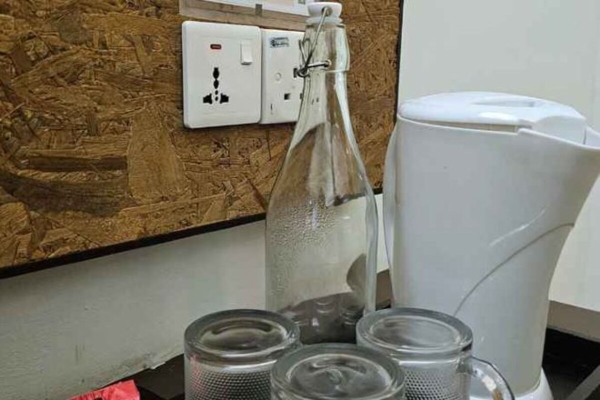Une pièce avec une machine à café blanche, une bouteille en verre et trois récipients en verre posés sur un comptoir.