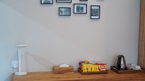 Un escritorio de madera con una caja de pañuelos, paquetes de snacks, un hervidor y una cafetera.