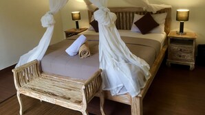 Una cama con dosel, dos mesitas de noche con lámparas, un banco de madera y una mesita auxiliar de madera.