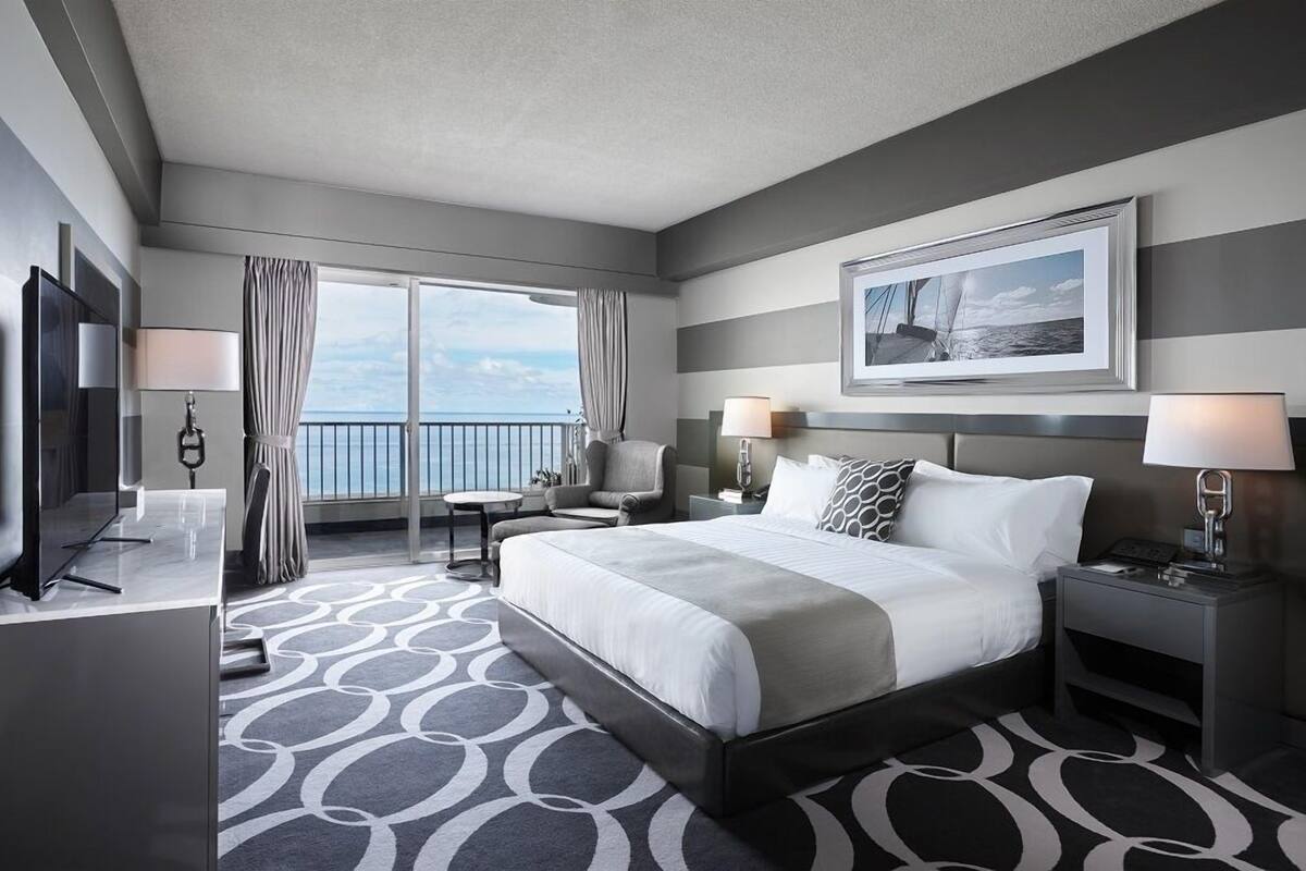 Een hotelkamer met een groot bed, een televisie, een bureau en uitzicht op de oceaan.