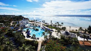 A resort with a large pool, palm trees, and a beach view.