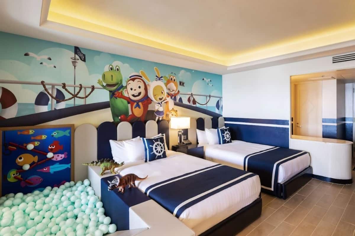 Een hotelkamer met twee bedden, een bällebak en een muurschildering met tekenfilmfiguren.