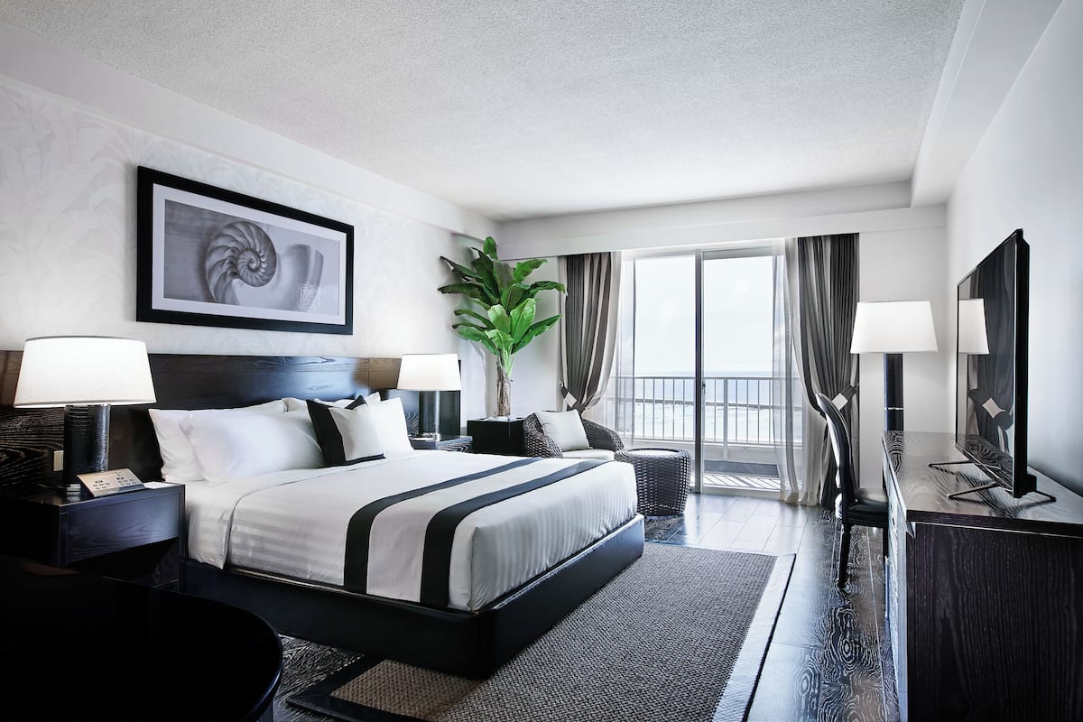 Een moderne hotelkamer met een groot bed, nachtkastjes met lampen, een grote spiegel en uitzicht op het omliggende landschap.