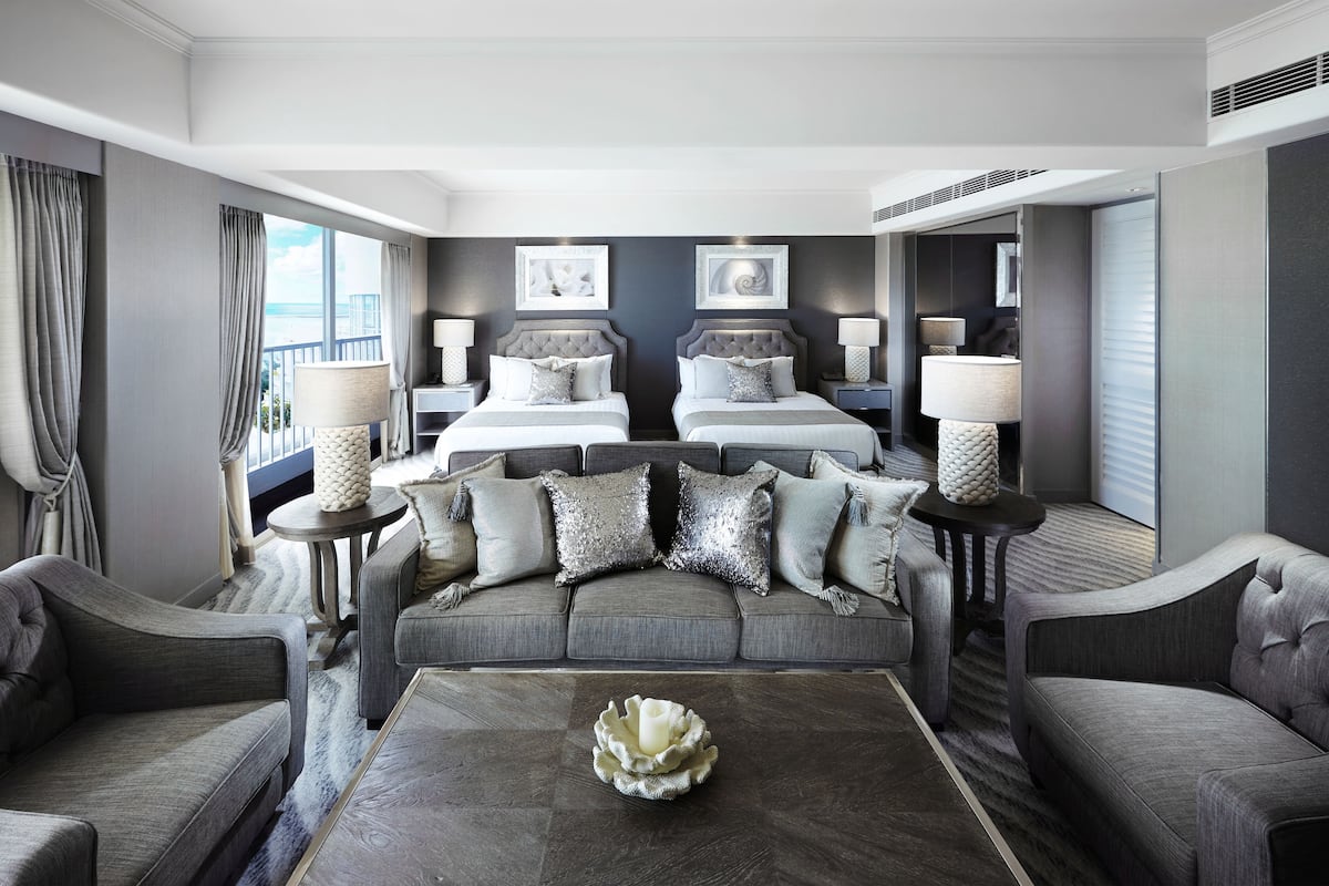 Een hotelkamer met twee bedden, een bank, een bijzettafeltje en uitzicht op zee.