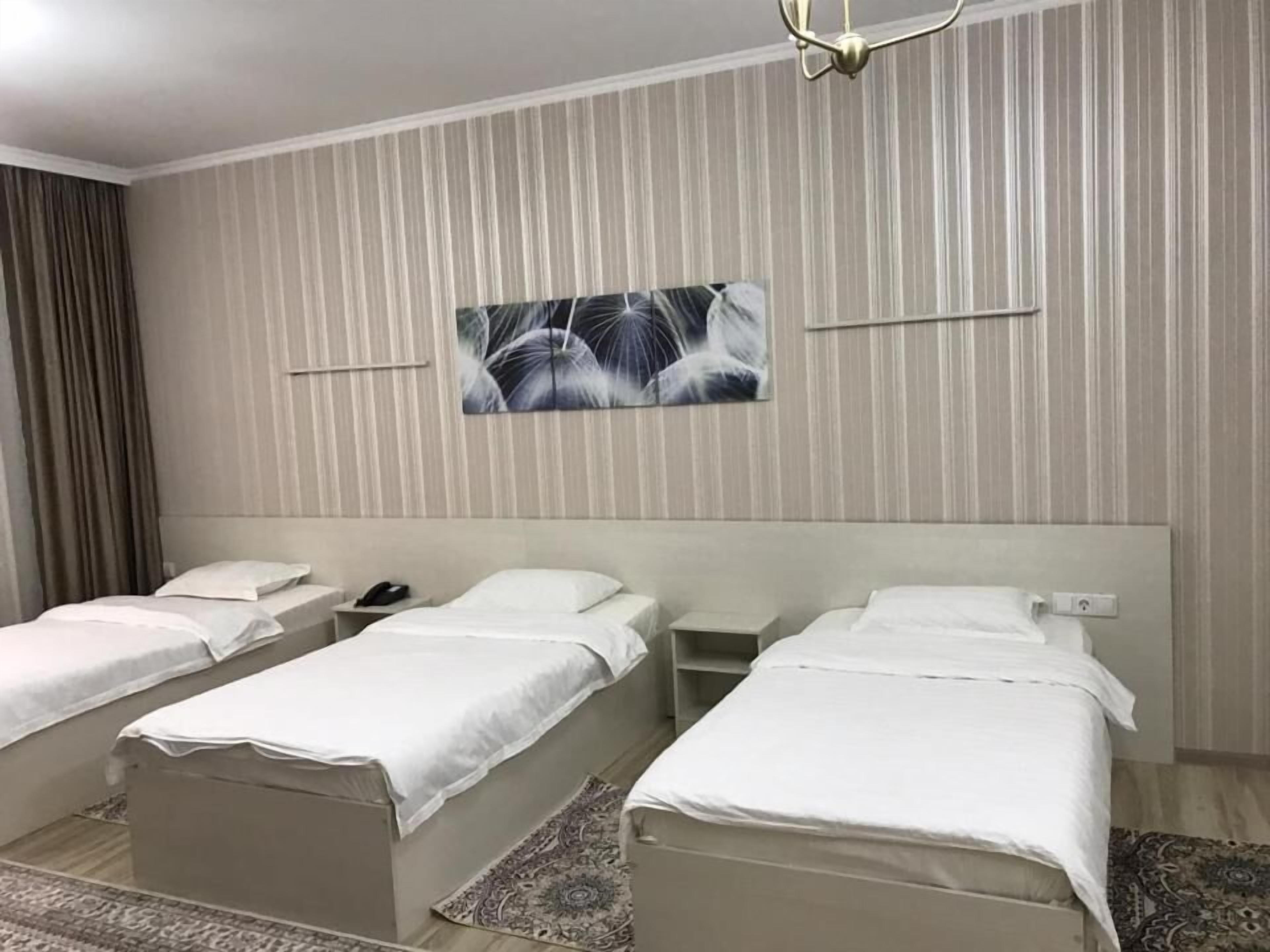 A hotel room with two single beds, a nightstand with a phone, a wall-mounted painting, and a patterned rug.