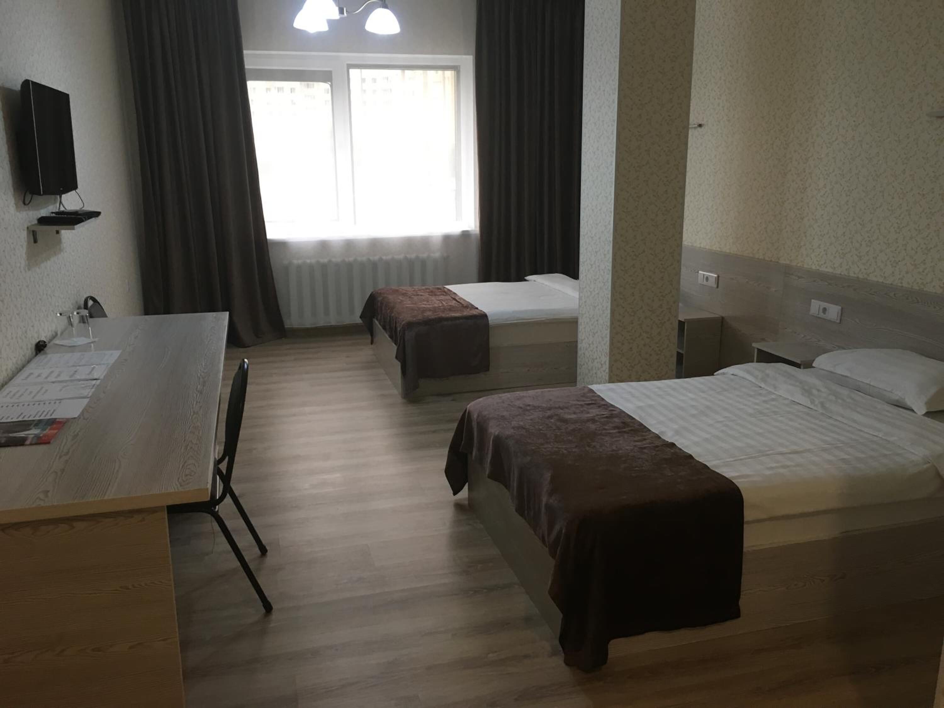Habitación de hotel con dos camas, un escritorio con computadora y una ventana con cortinas.