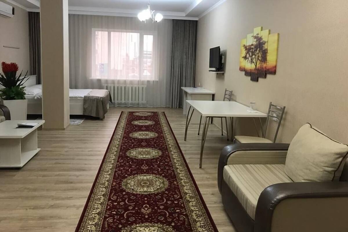 A modern living room with a dining area, a sofa, a coffee table, a TV, and a large window with curtains.