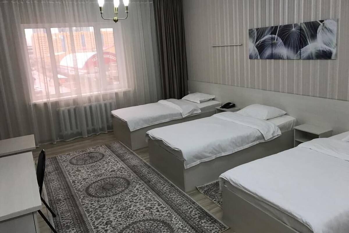 A hotel room with two single beds, a desk, a chair, a patterned rug, a chandelier, and a window with curtains.