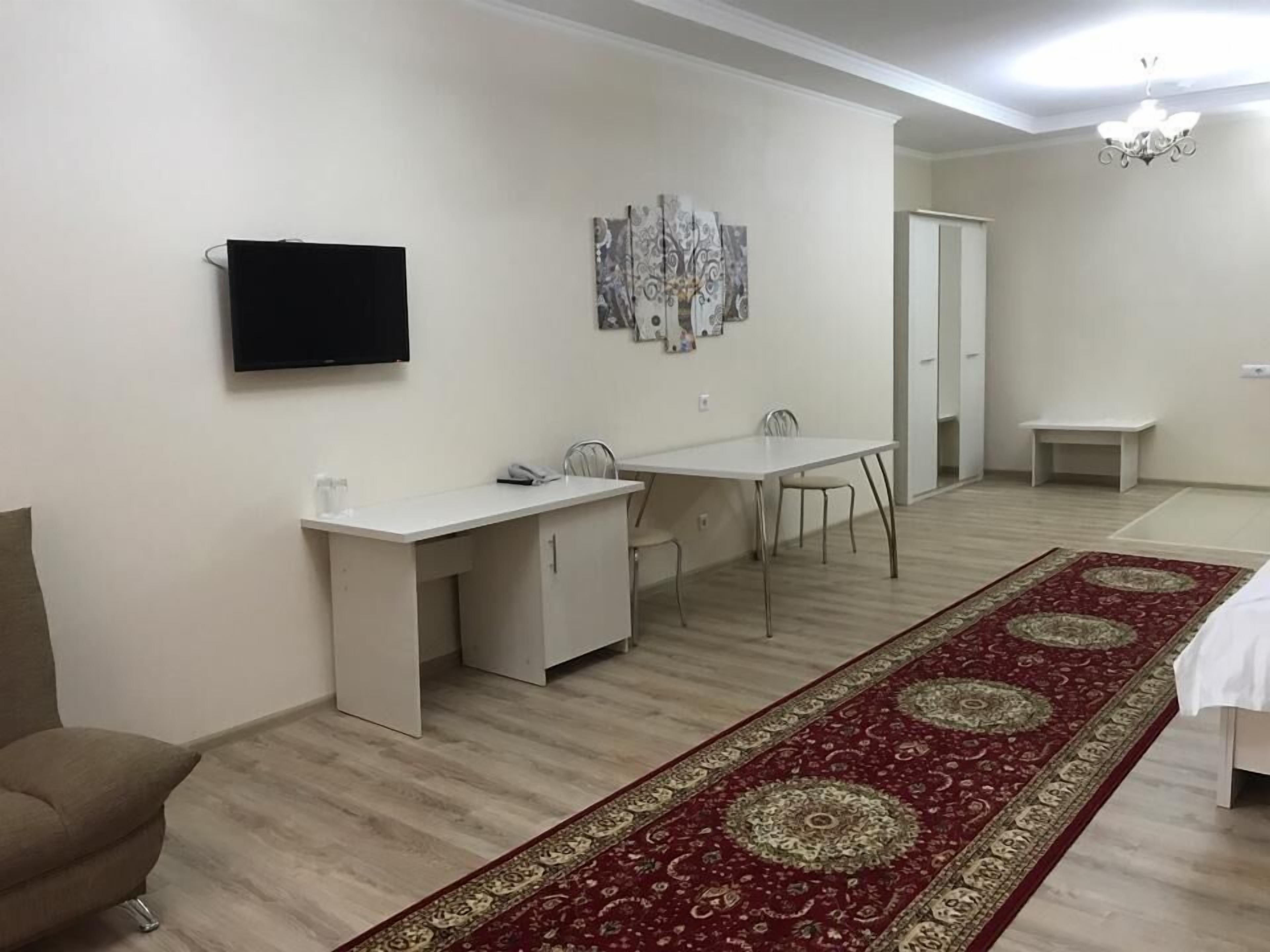 A room with a dining table, chairs, a TV mounted on the wall, and a patterned rug on the floor.