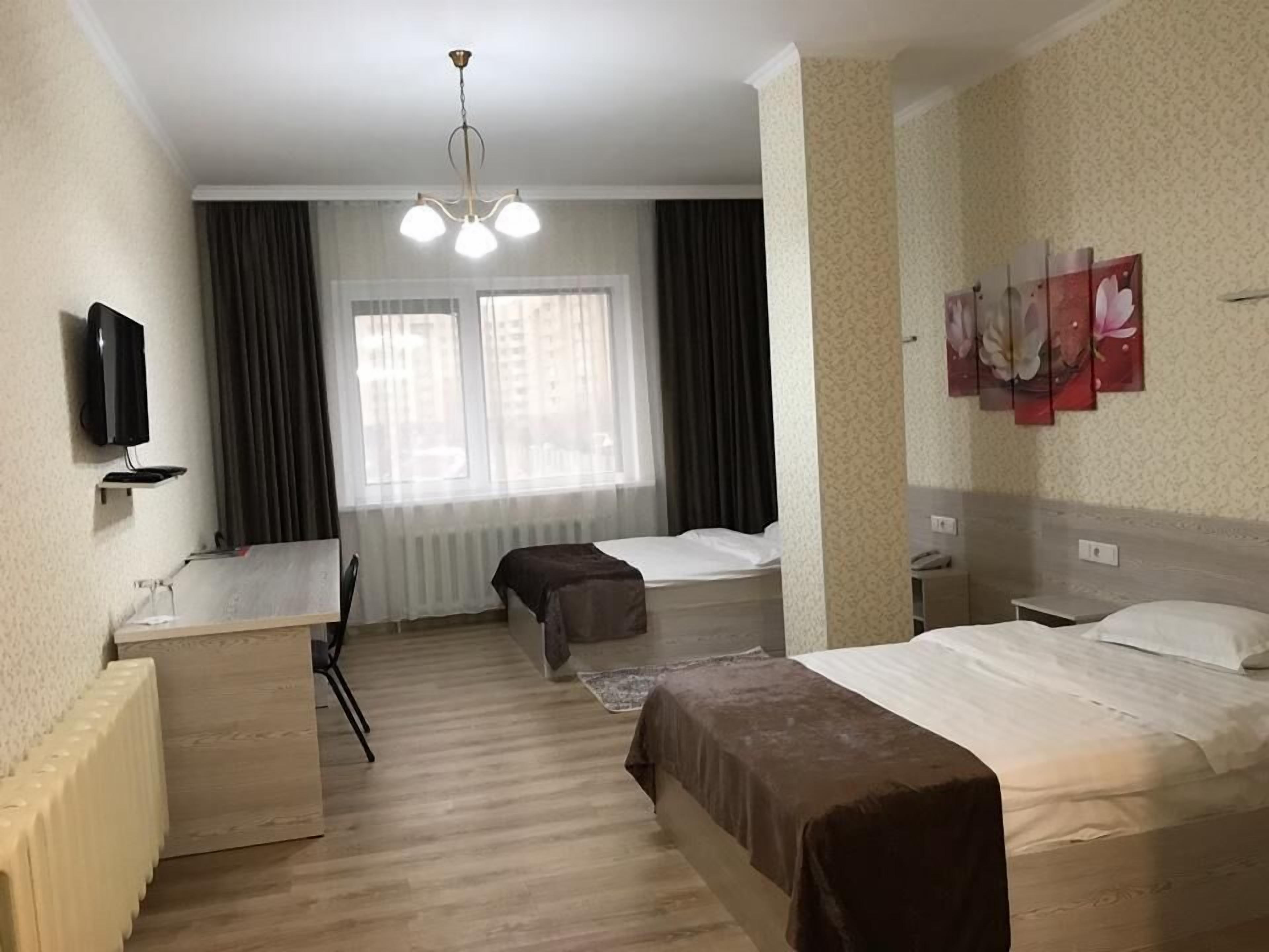 Hotelkamer met twee bedden, een bureau, een stoel, een televisie en een raam met gordijnen.