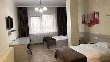 Habitación de hotel con dos camas, un escritorio, una silla, un televisor y una ventana con cortinas.