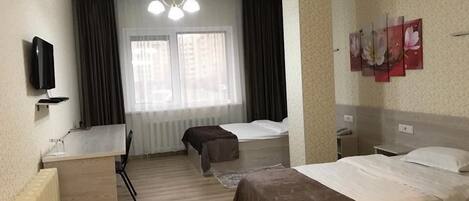 Habitación de hotel con dos camas, un escritorio, una silla, un televisor y una ventana con cortinas.