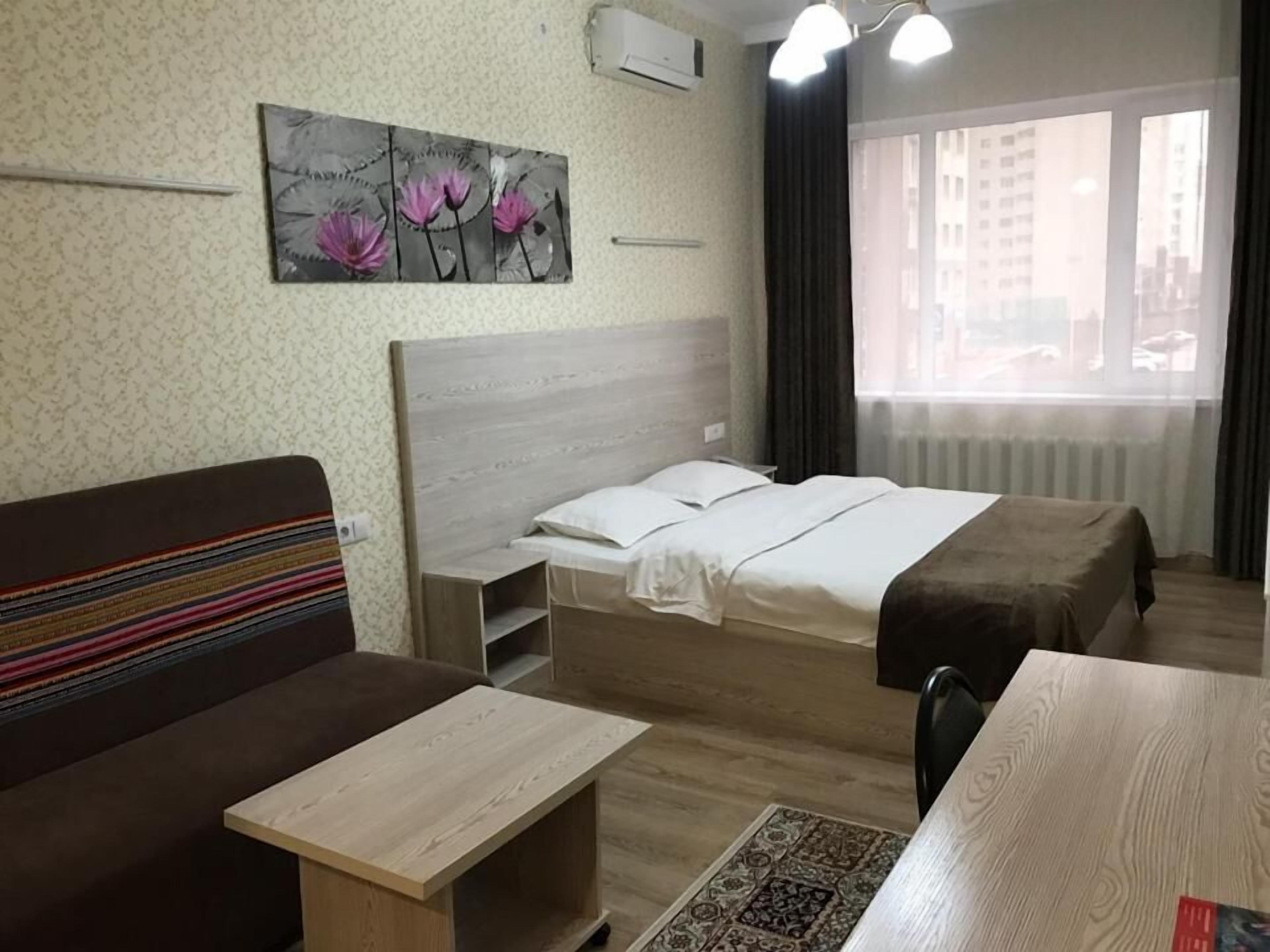 A hotel room with a bed, a sofa, a small table, and a painting of flowers on the wall.