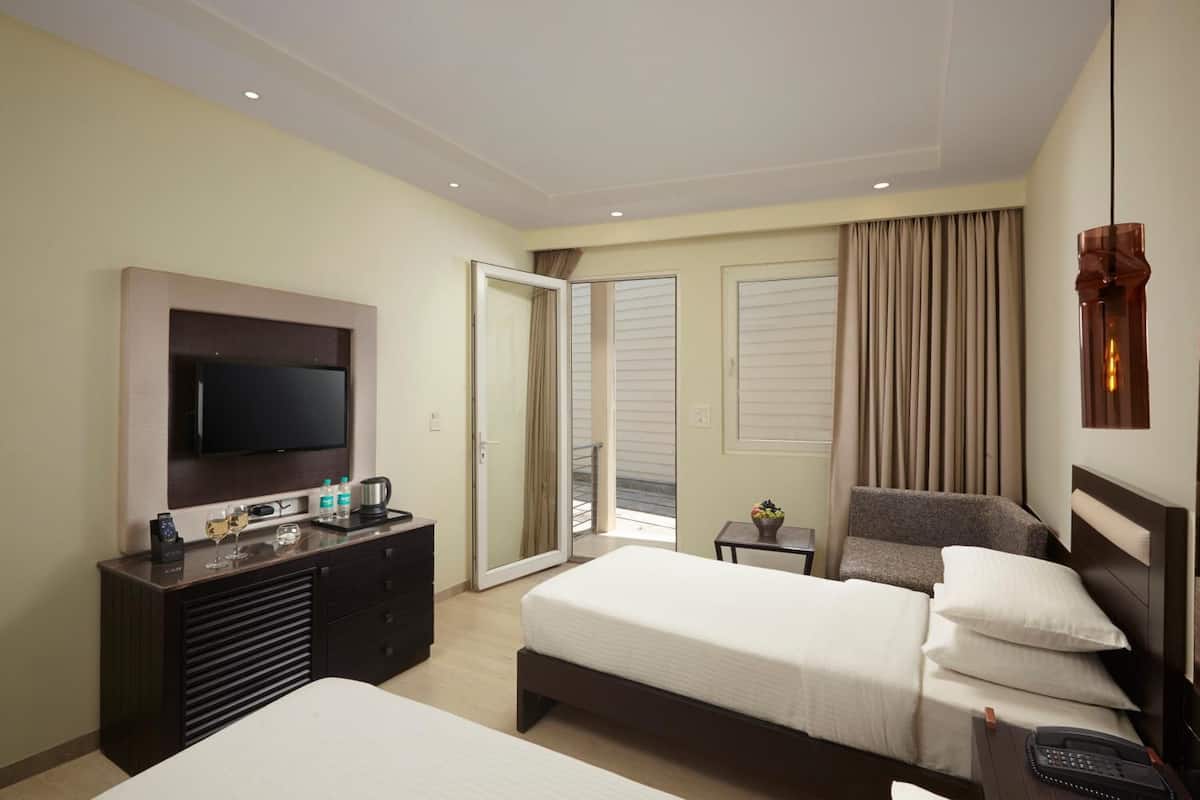 A hotel room with a bed, a desk, a TV, and a balcony with curtains.