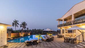 A pool area with lounge chairs, a dining area, and a staircase leading to an upper level. - Acacia Resort & Spa Morjim Goa (Morjim)