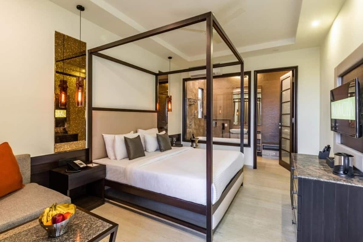 A four-poster bed in a modern hotel room with a sofa, bedside table, and a fruit bowl.