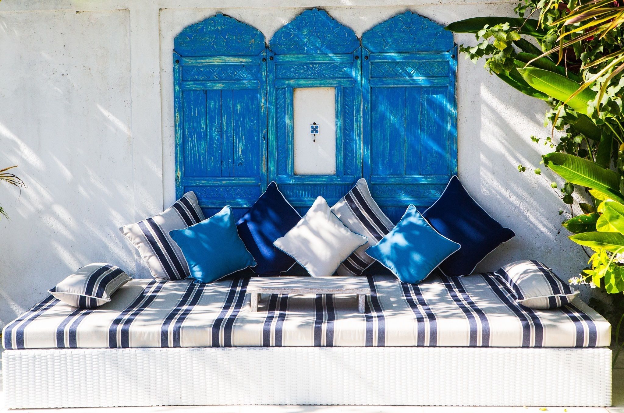 A white wicker sofa with striped cushions and a blue door in the background.