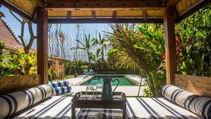 A poolside seating area with a view of a swimming pool, surrounded by lush tropical plants.
