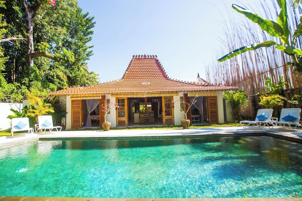 Área de piscina com cobertura em azulejos, espreguiçadeiras e plantas em vasos.