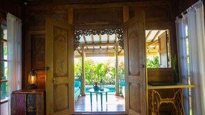 A wooden room with a view of a garden, a table with chairs, and a small cabinet with a lantern.