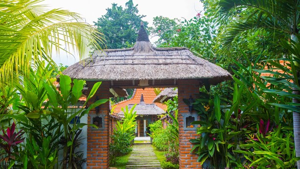 A traditional thatched-roof structure with a brick base, surrounded by lush tropical vegetation.