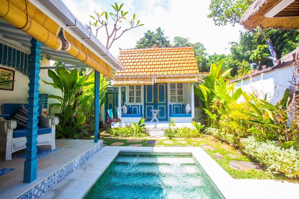 Uma área de piscina com deck azul e branco, uma piscina pequena e vegetação exuberante ao redor.