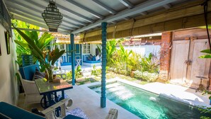 A covered outdoor area with a pool, seating, and potted plants.