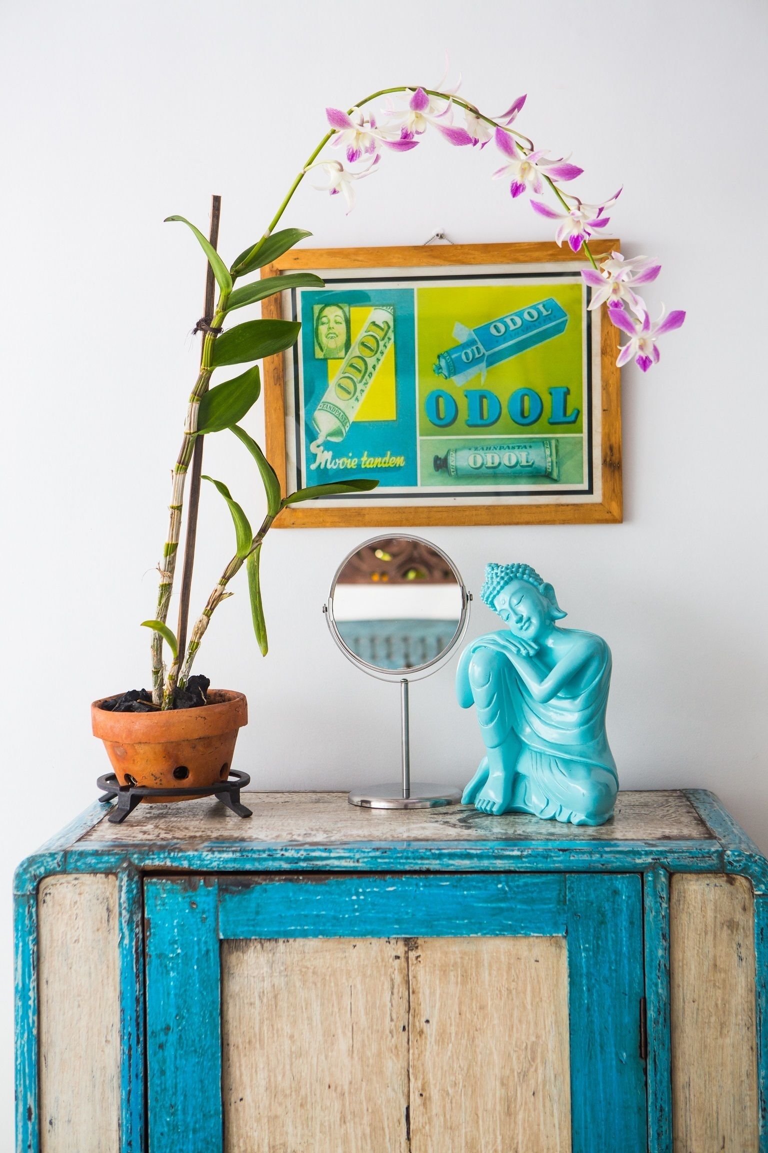 Ein blauer Schrank mit Buddha-Statue, einer Topfpflanze und einem gerahmten Filmplakat.