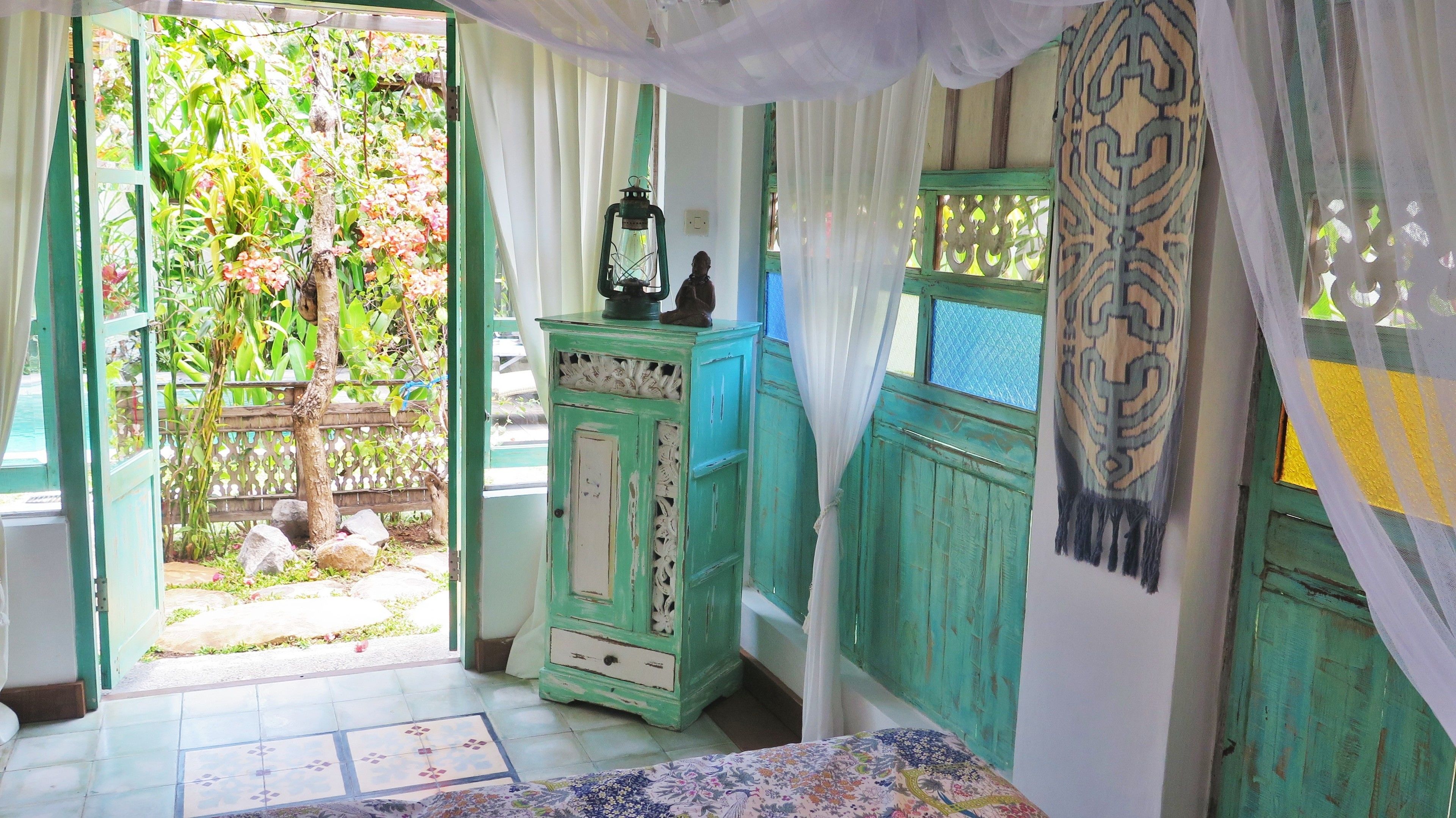 A room with a view of a garden, a green cabinet, and a patterned wall hanging.