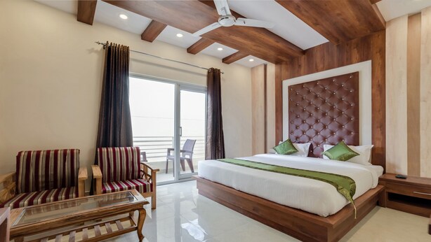 Habitación de hotel con una cama grande, dos sillones a rayas, una mesa de centro de vidrio y un balcón con vistas.