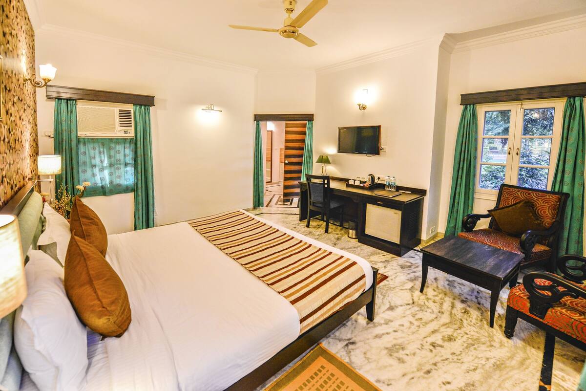 Habitación de hotel con cama, escritorio, silla, televisor y ventilador de techo.