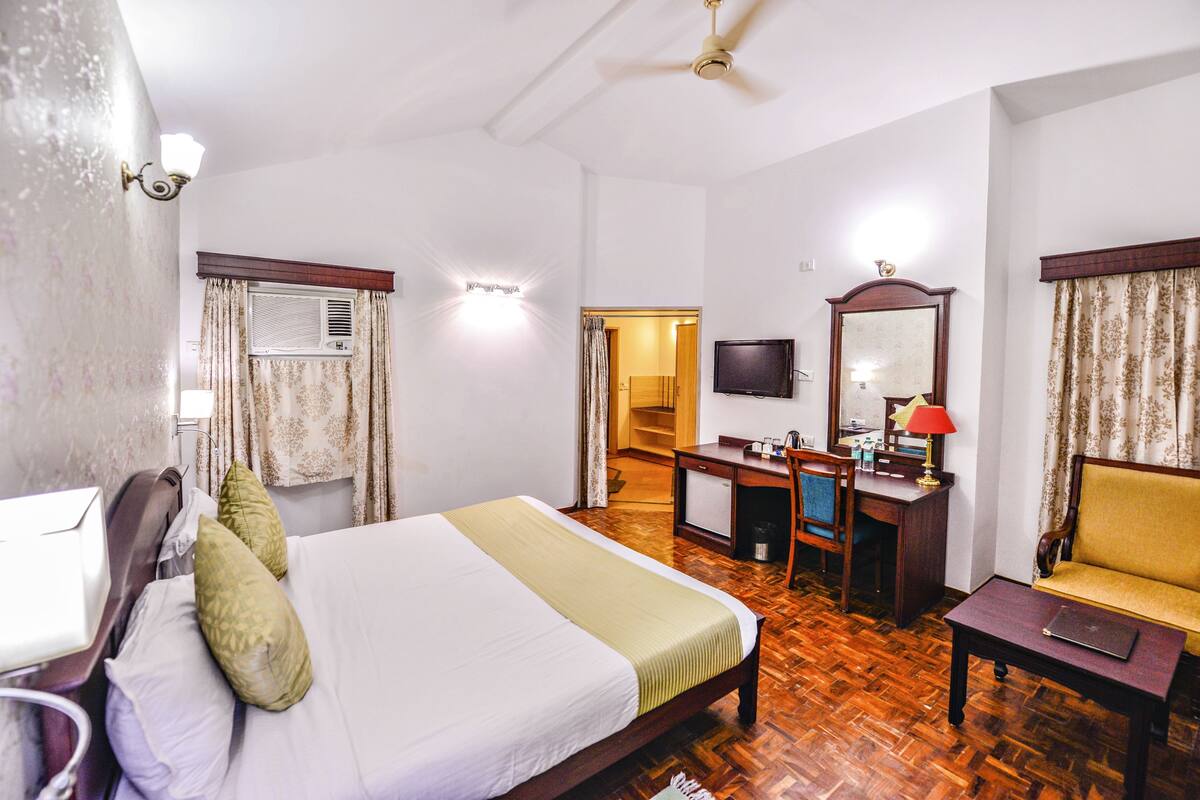 Una habitación de hotel con cama, escritorio, silla, televisor y ventilador de techo.