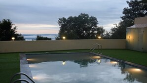 Una piscina con una escalera de metal, rodeada de césped verde y un muro bajo.
