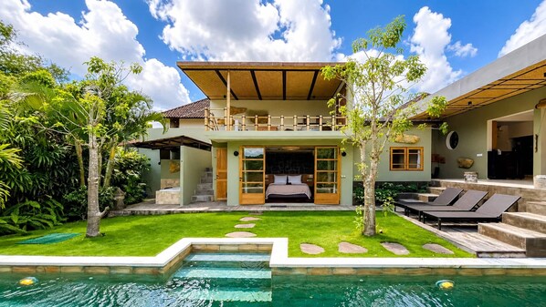 A two-story house with a swimming pool, a balcony, and a garden.