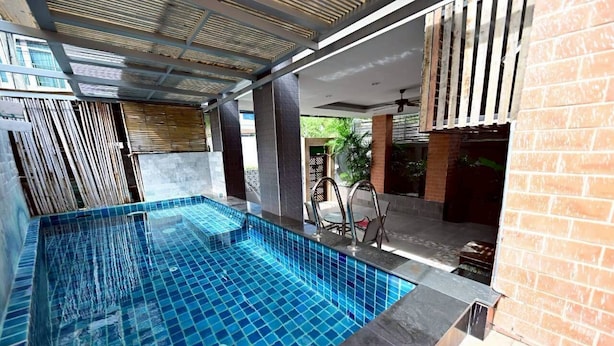A modern indoor swimming pool with clear blue tiles, surrounded by a brick wall and a ceiling with a unique slatted design.