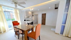 A modern kitchen with white cabinets, a dining area with a wooden table and orange chairs, and a ceiling fan.