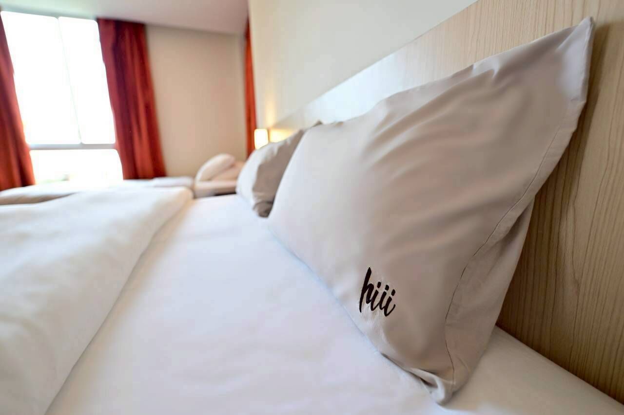 A neatly made bed with white linens and a pillow with the word "hiii" on it.
