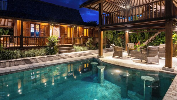 Un área de piscina con terraza de madera, sillas de descanso y una zona de estar cubierta.