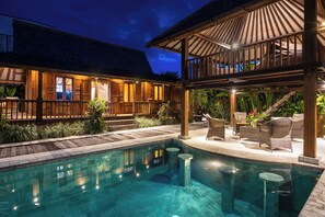 Un espace piscine doté d’une terrasse en bois, de chaises longues et d’un coin salon abrité.
