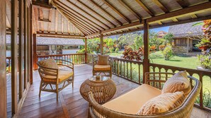 Una terraza de madera con mobiliario de mimbre y vistas a un jardín.