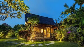 Una casa de madera tradicional con techo de tejas, rodeada de abundante vegetación y un sendero de piedra que conduce a la entrada.
