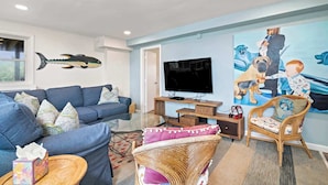 Ein Wohnzimmer mit einem blauen Sofa, einem Fernseher und einem Bild von Hunden und einem Kind.