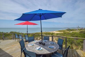 A wooden deck with a round table set for four, two umbrellas, and chairs. - Gorgeous Architectural Waterfront Property! (Eastham)