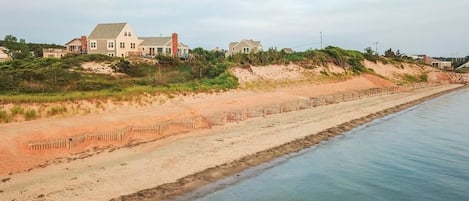A coastal property with a sandy beach, a wooden fence, and a large house with a sloped roof.