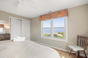 Een slaapkamer met een groot bed, een raam met uitzicht op het strand, een kledingkast en een stoel.