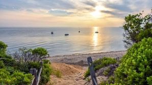 Ein Strand mit einer Holzbrüstung, die zum Ufer führt, einem sandigen Pfad und Booten auf dem Wasser.